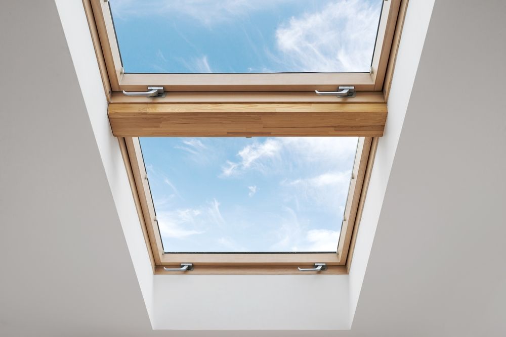 Tragaluz con moldura de madera, abierto a un cielo azul brillante con nubes.