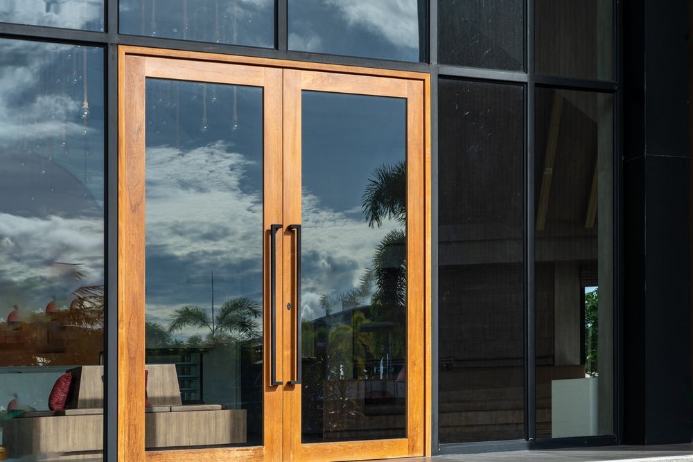 Puertas dobles de madera con paneles de vidrio; reflejos de cielo y árboles.