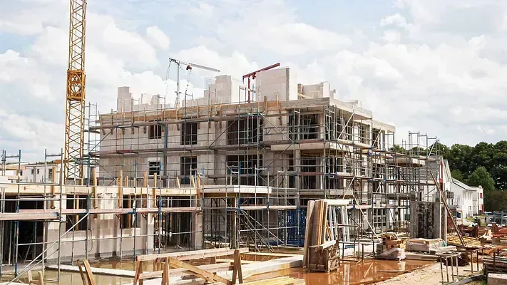 Un gran edificio en construcción con andamios y una grúa al fondo.