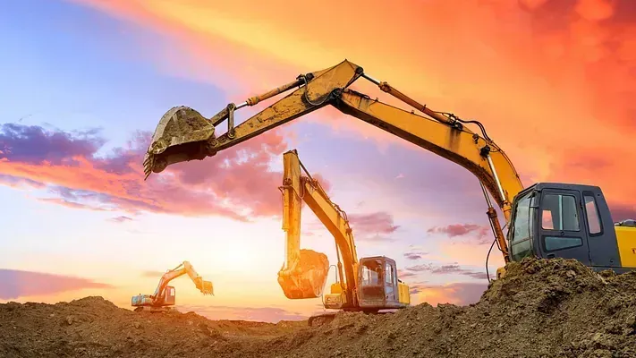 Dos excavadoras están trabajando en un sitio de construcción al atardecer.