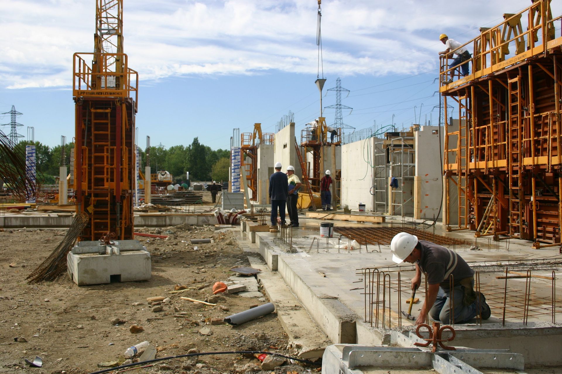 Chantier de construction avec ouvriers, échafaudages et coffrages en béton sous un ciel bleu