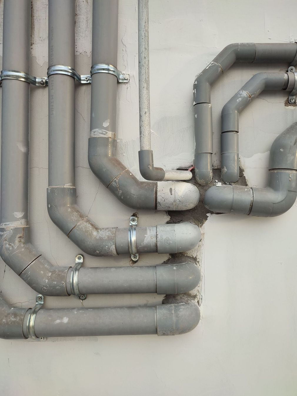 Des tuyaux métalliques gris, avec des joints et des coudes, courbés verticalement et horizontalement le long d'un mur.