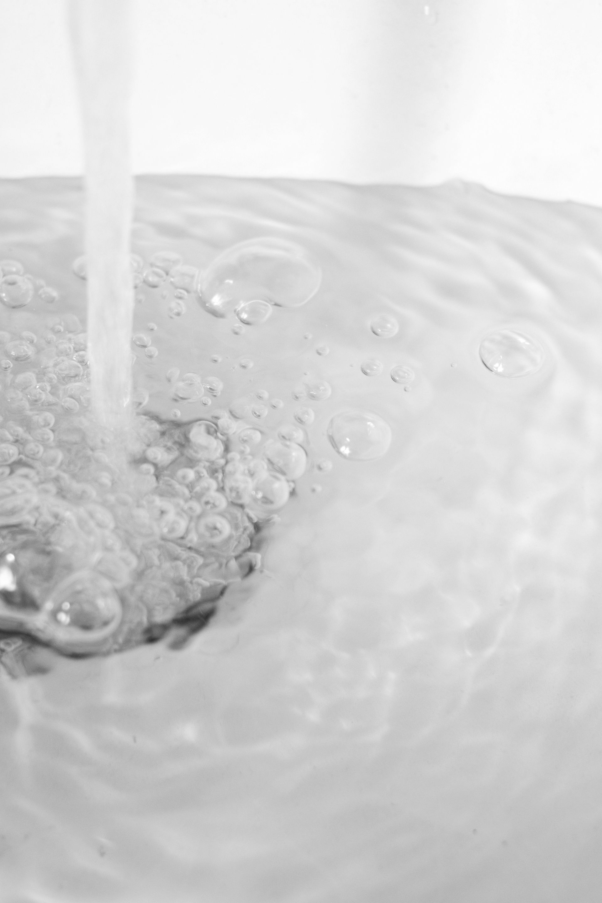 De l'eau se déverse dans un lavabo blanc, créant des bulles et des tourbillons d'écume.