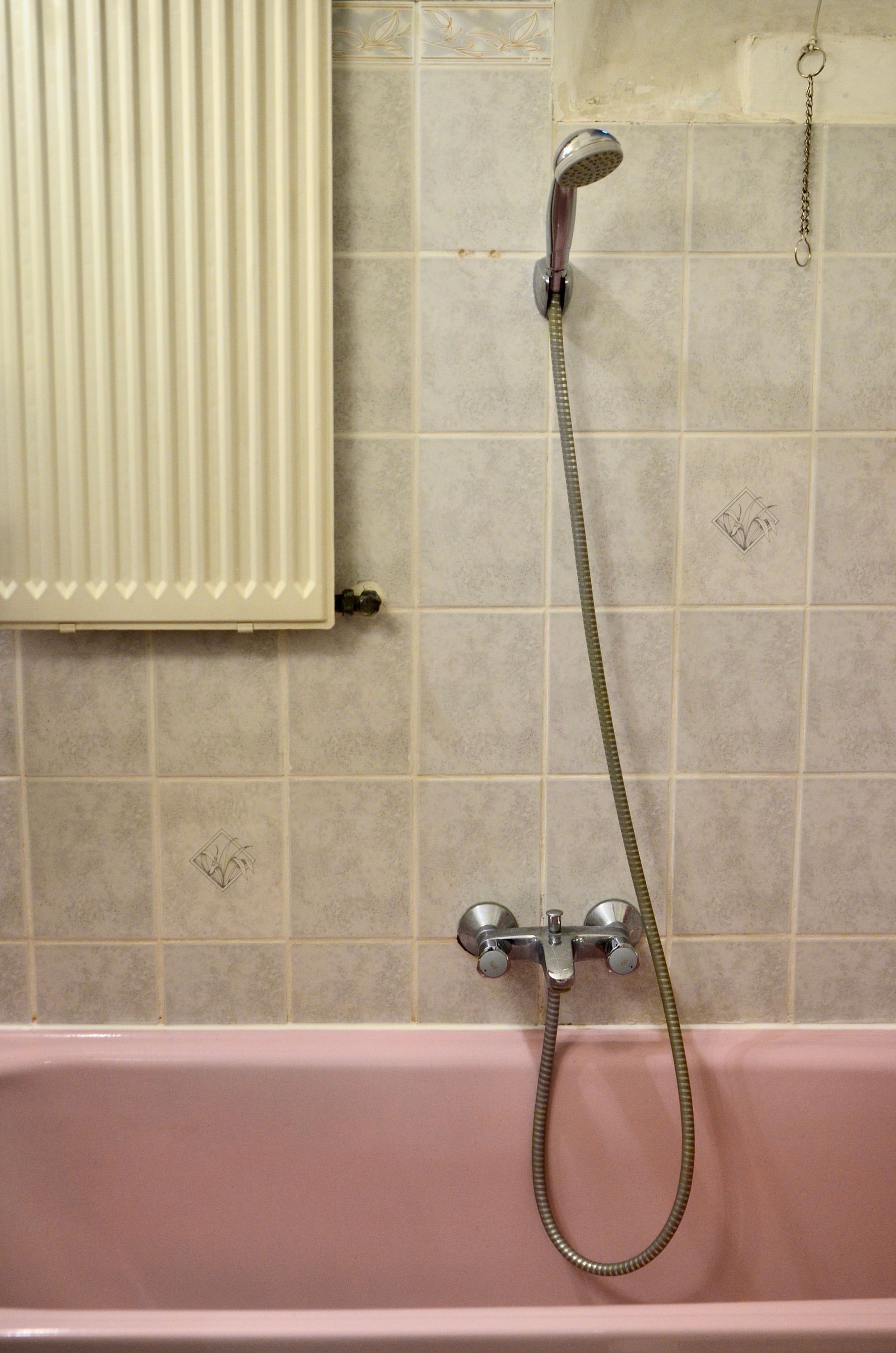 Baignoire rose avec douchette et mur de salle de bains carrelé beige à côté d'un radiateur