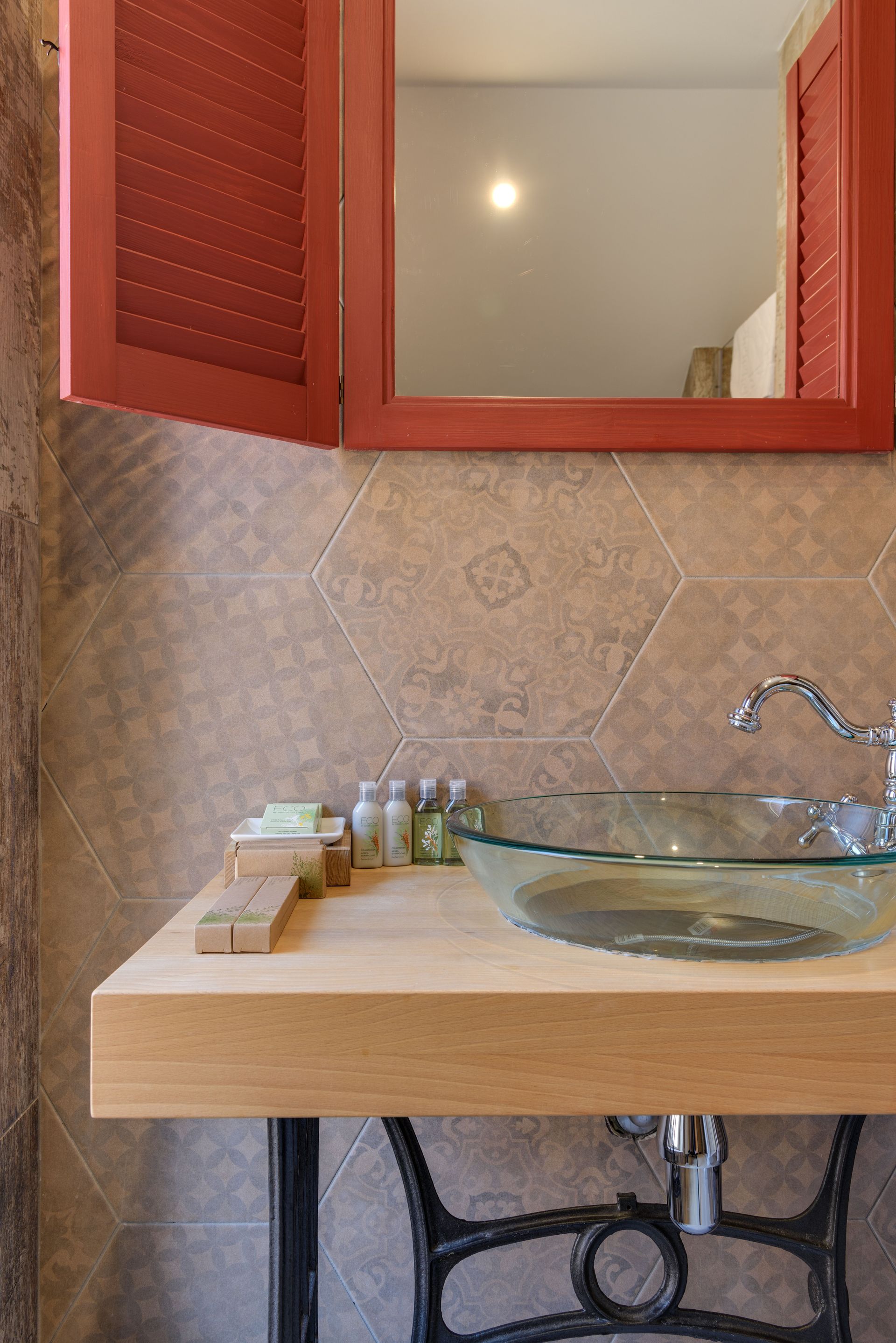 Meuble-lavabo de salle de bains avec comptoir en bois, lavabo en verre et armoire à miroir rouge au-dessus d'un mur carrelé.