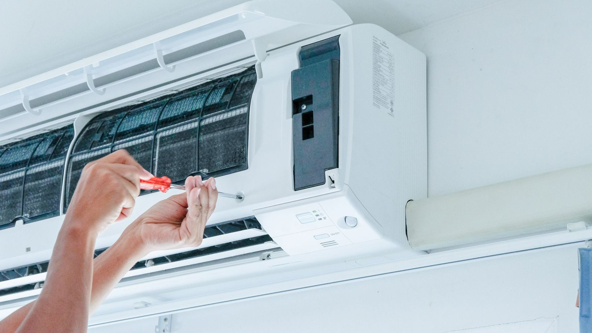 Un technicien répare un climatiseur avec un tournevis