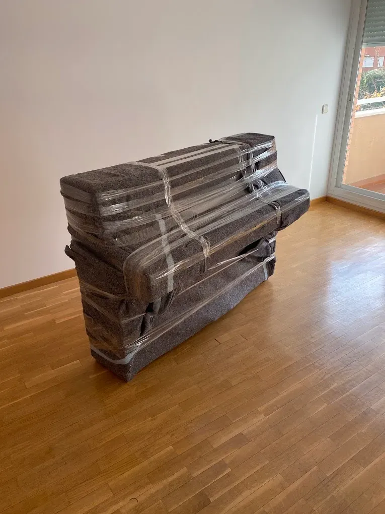 Muebles envueltos apilados sobre un suelo de madera en una habitación vacía cerca de una ventana.