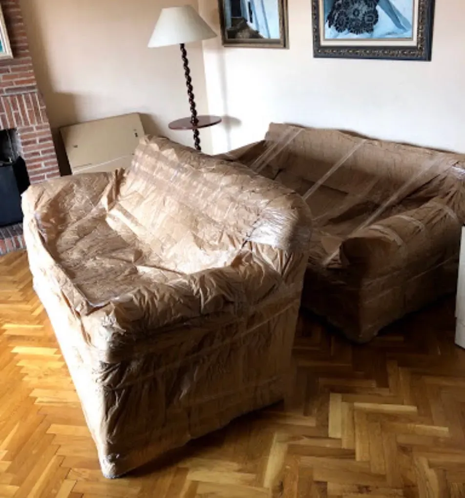 Dos sofás embaladas en una sala de estar con pisos de madera, una lámpara y cuadros enmarcados en la pared.