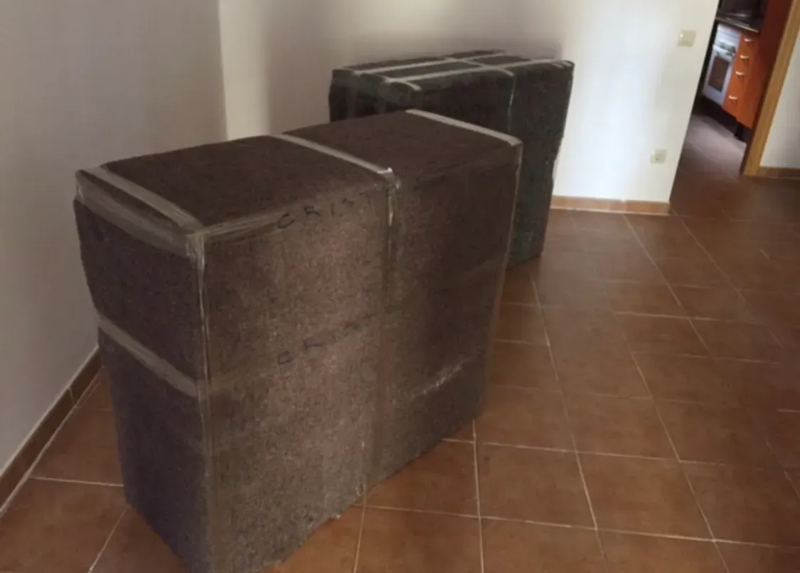Dos muebles embalados con mantas están alineadas a lo largo de una pared alicatada del pasillo.