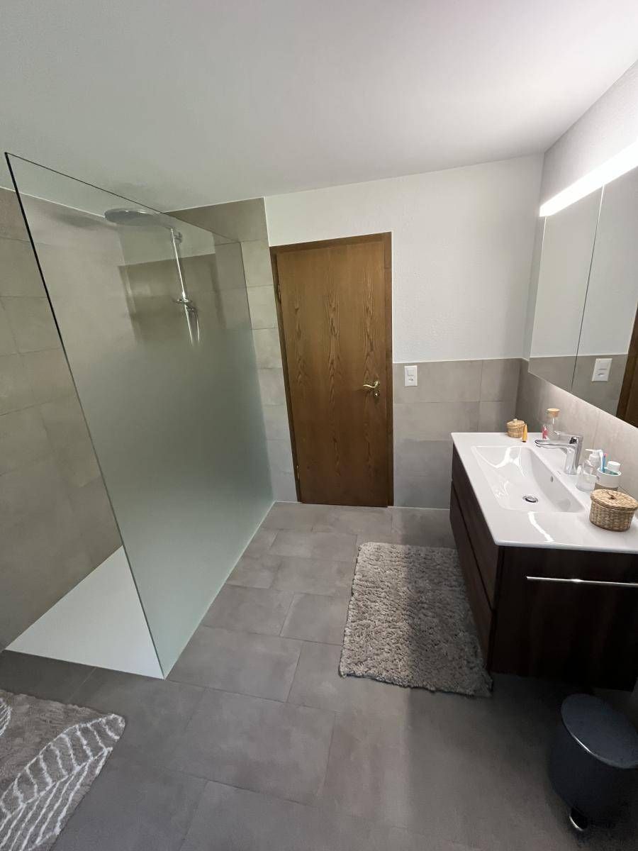 Modernes Badezimmer mit Glasdusche, Holztür und Waschtisch mit zwei Waschbecken.