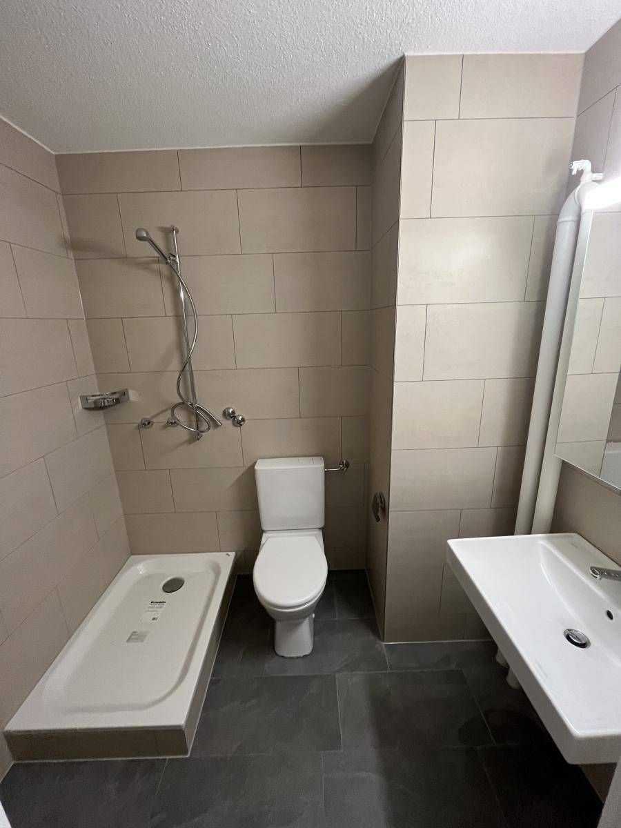 Badezimmer mit hellbraun gefliesten Wänden, Dusche, Toilette und Waschbecken.