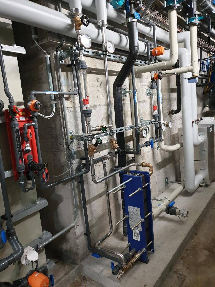 Rohre und Messgeräte, die in einer Industrieanlage an einer Betonwand montiert sind.