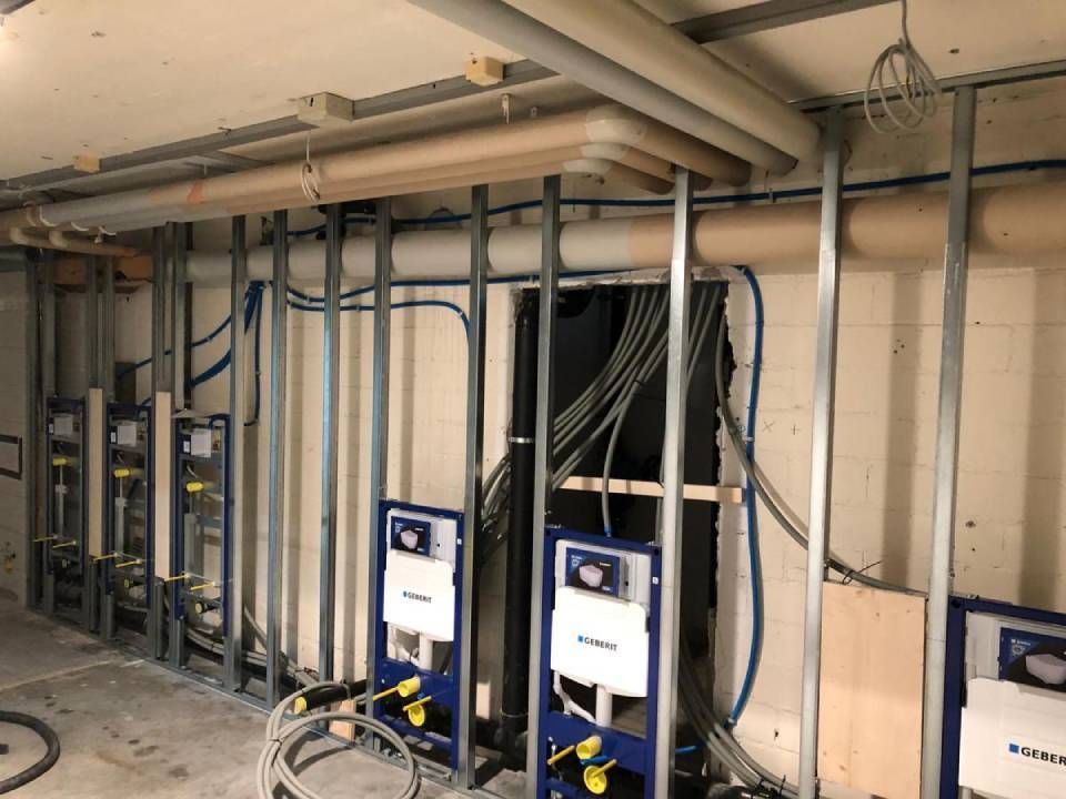 Bau einer Badezimmerwand, wobei die Sanitär- und Elektroinstallationen sichtbar sind.