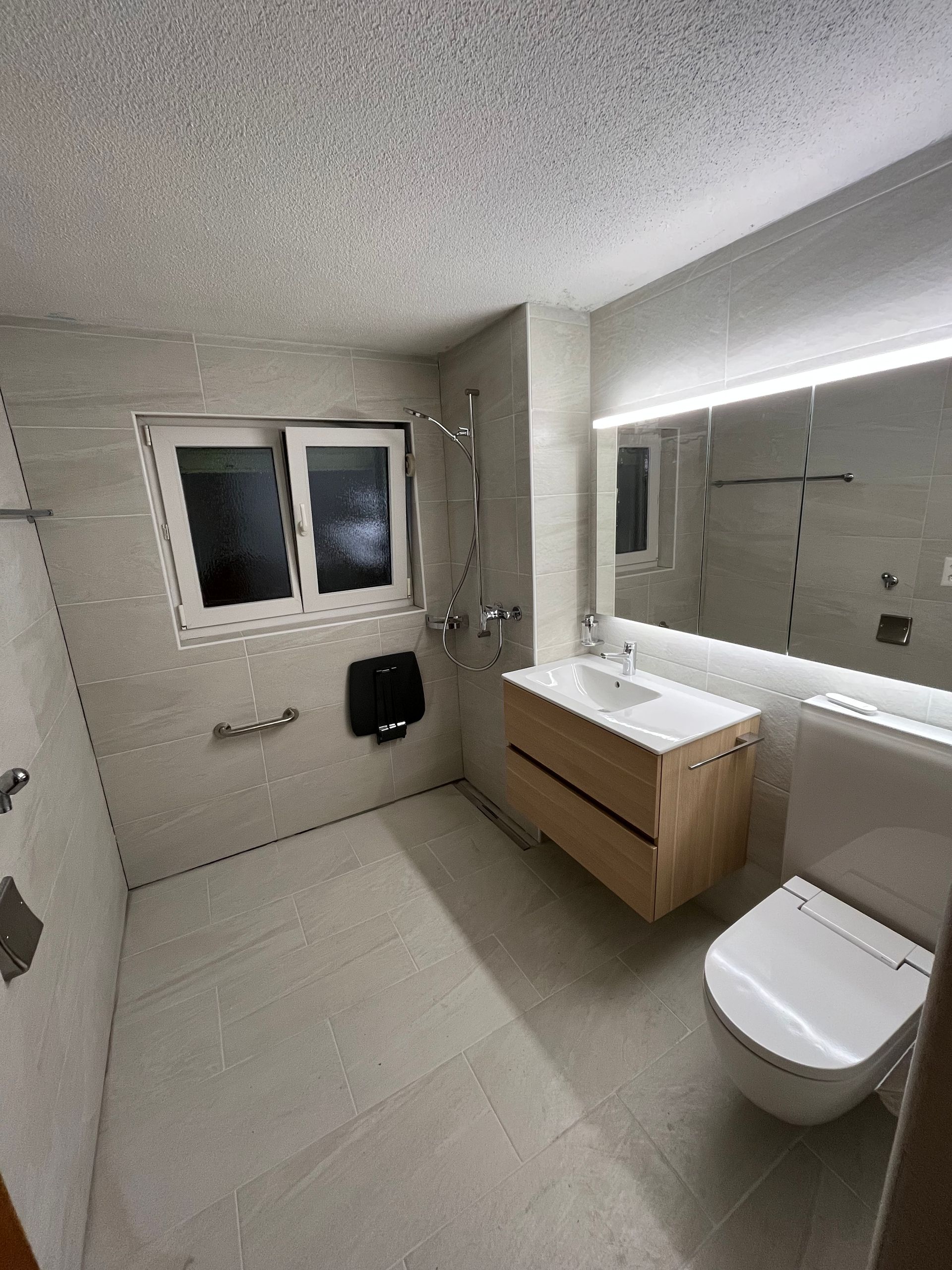 Badezimmer mit hellbraun gefliesten Wänden, Dusche, Toilette und Waschbecken.