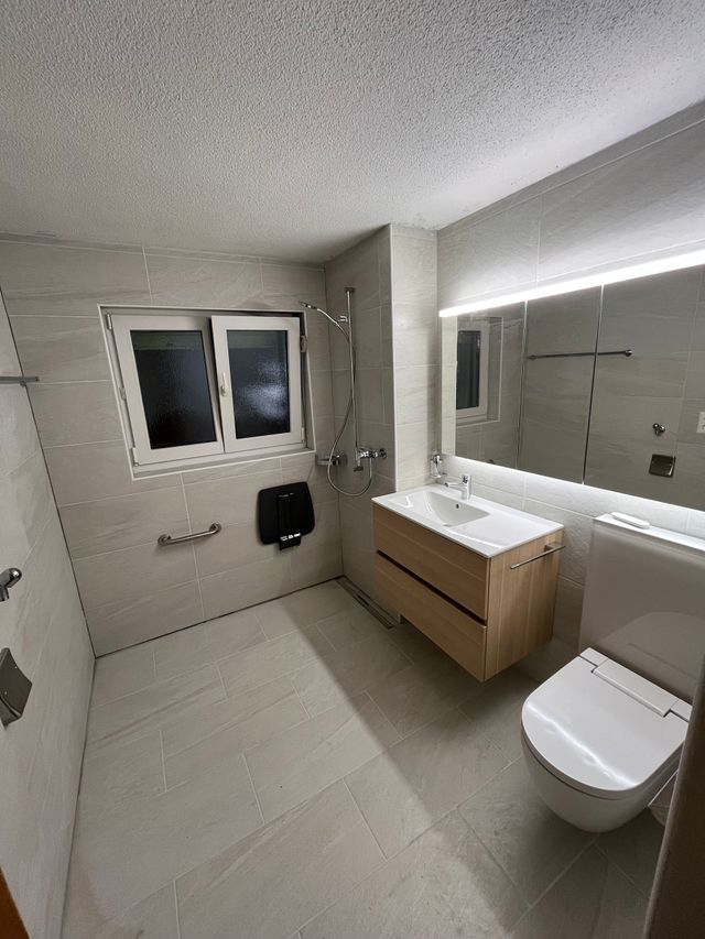 Badezimmer mit hellbraun gefliesten Wänden, Dusche, Toilette und Waschbecken.