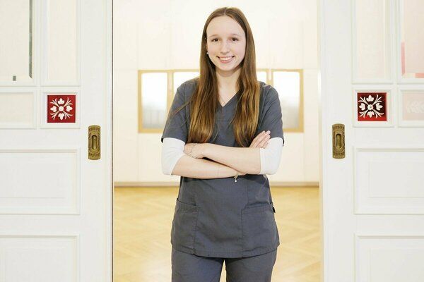 Eine Frau im OP-Kittel steht mit verschränkten Armen vor einer Tür.