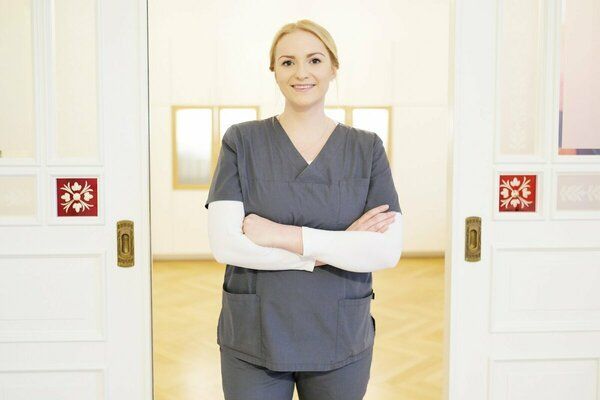 Eine Frau im OP-Kittel steht mit verschränkten Armen in einem Flur.