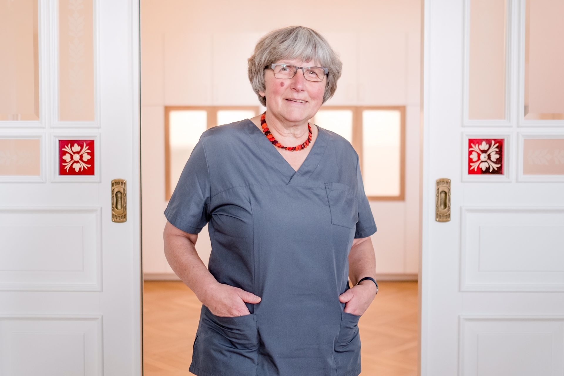 Eine Frau im OP-Kittel steht mit den Händen in den Taschen in einem Türrahmen.