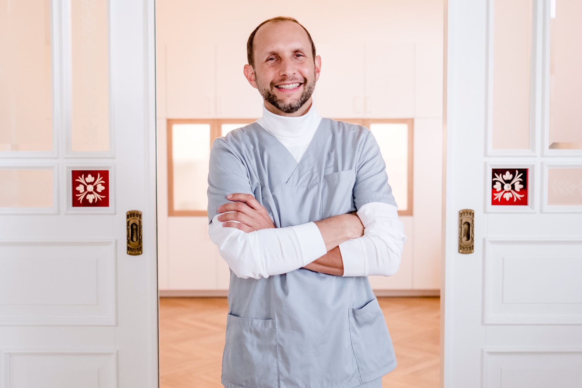Ein Mann im OP-Kittel steht mit verschränkten Armen vor einer Tür.