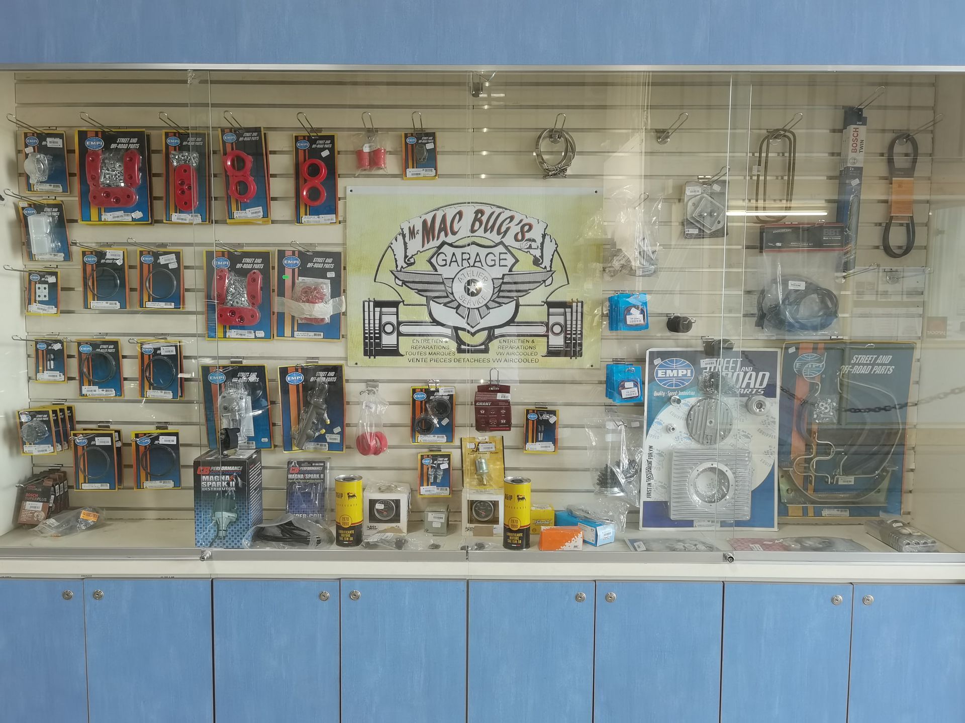 Mur d'exposition présentant des outils et des articles de quincaillerie, avec un logo central et des armoires bleues en dessous.