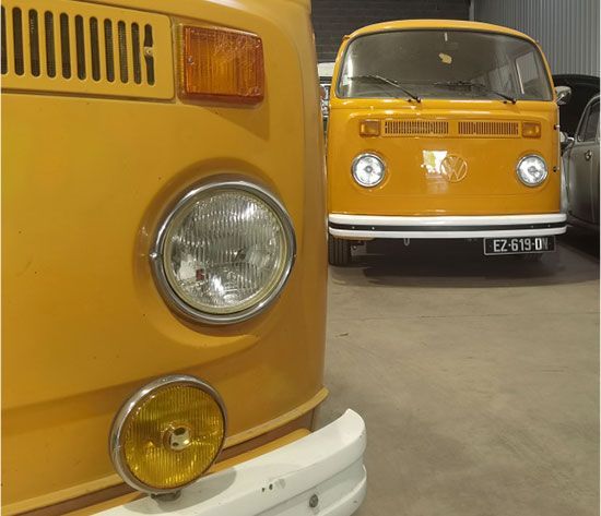 Deux fourgonnettes jaunes vintage garées à l'intérieur, un gros plan montrant les phares et les détails chromés.