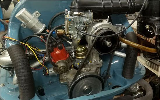 Compartiment moteur bleu avec moteur, courroies, durites et câblage apparents.