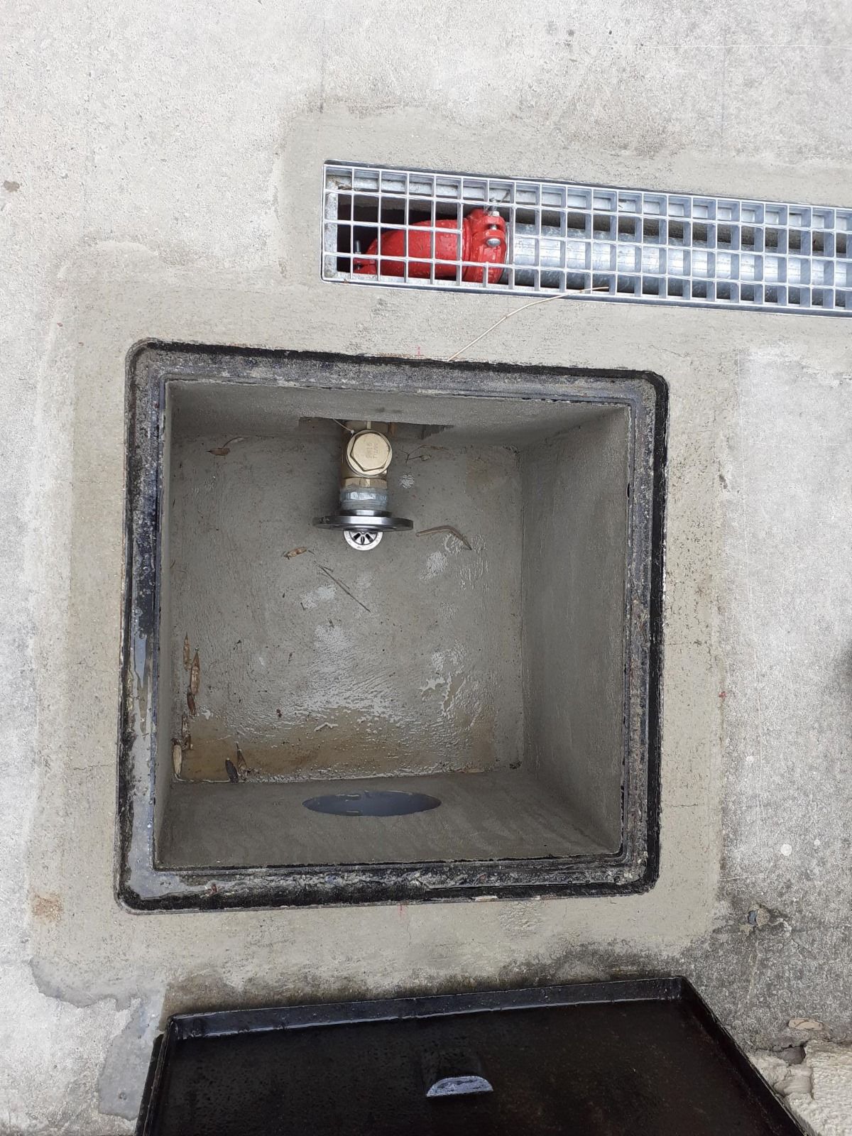 Una caja de hormigón con un desagüe y un grifo en su interior.