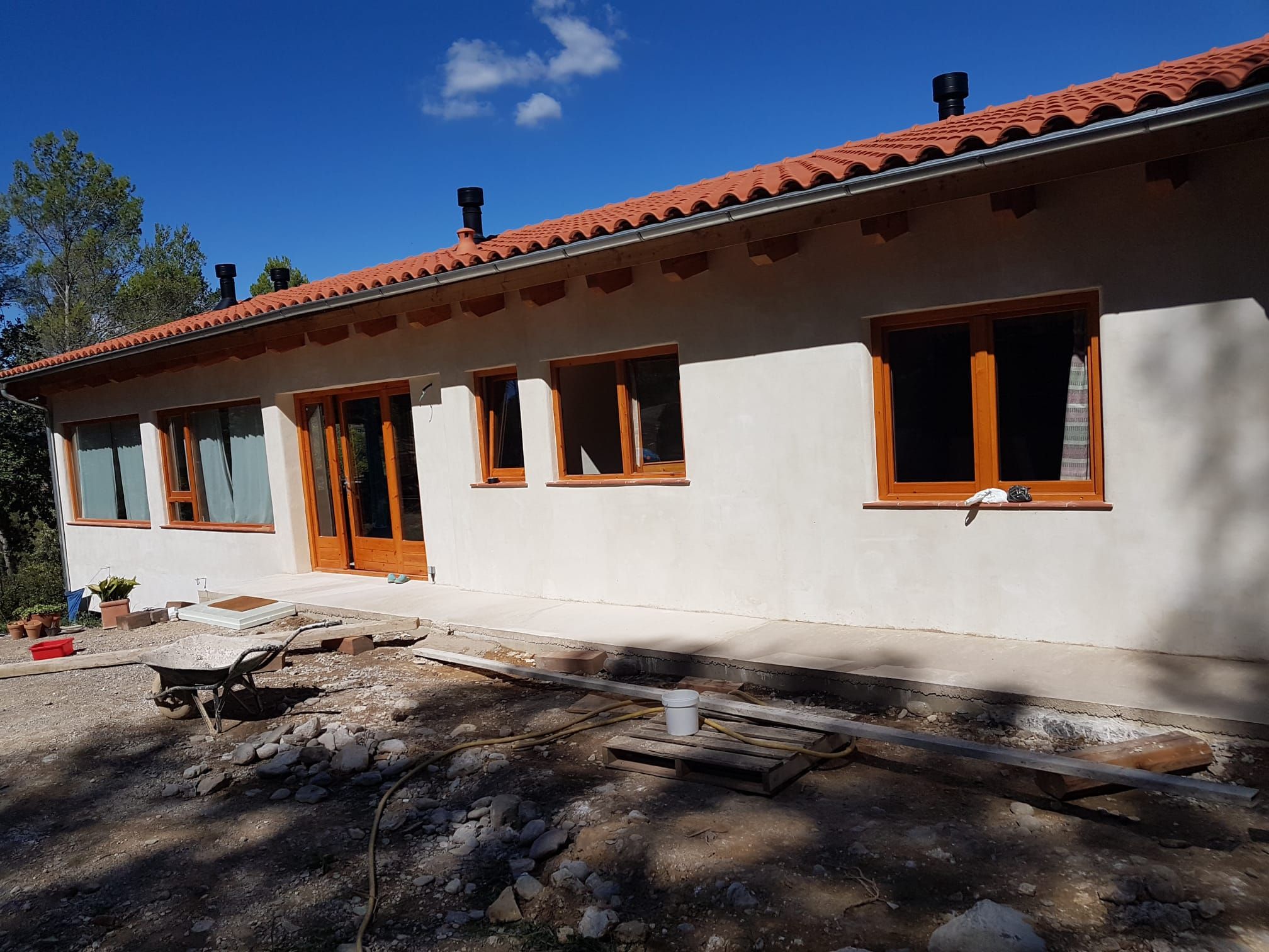 Una casa blanca con techo de tejas rojas tiene una carretilla delante.