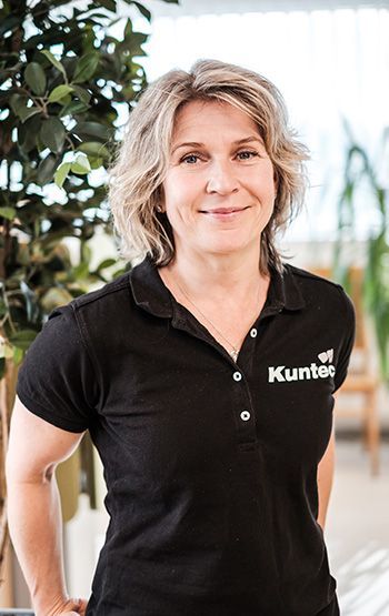 Hymyilevä henkilö mustassa poolopaidassa sisätiloissa kasvien lähellä