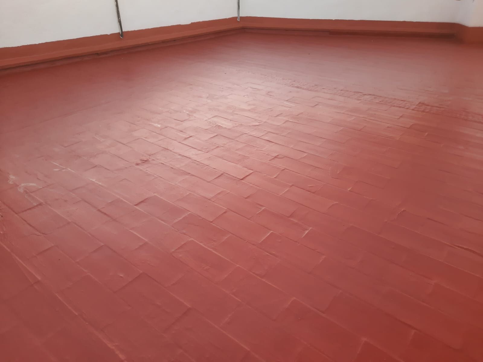 Un piso de ladrillo rojo con una pared blanca al fondo.
