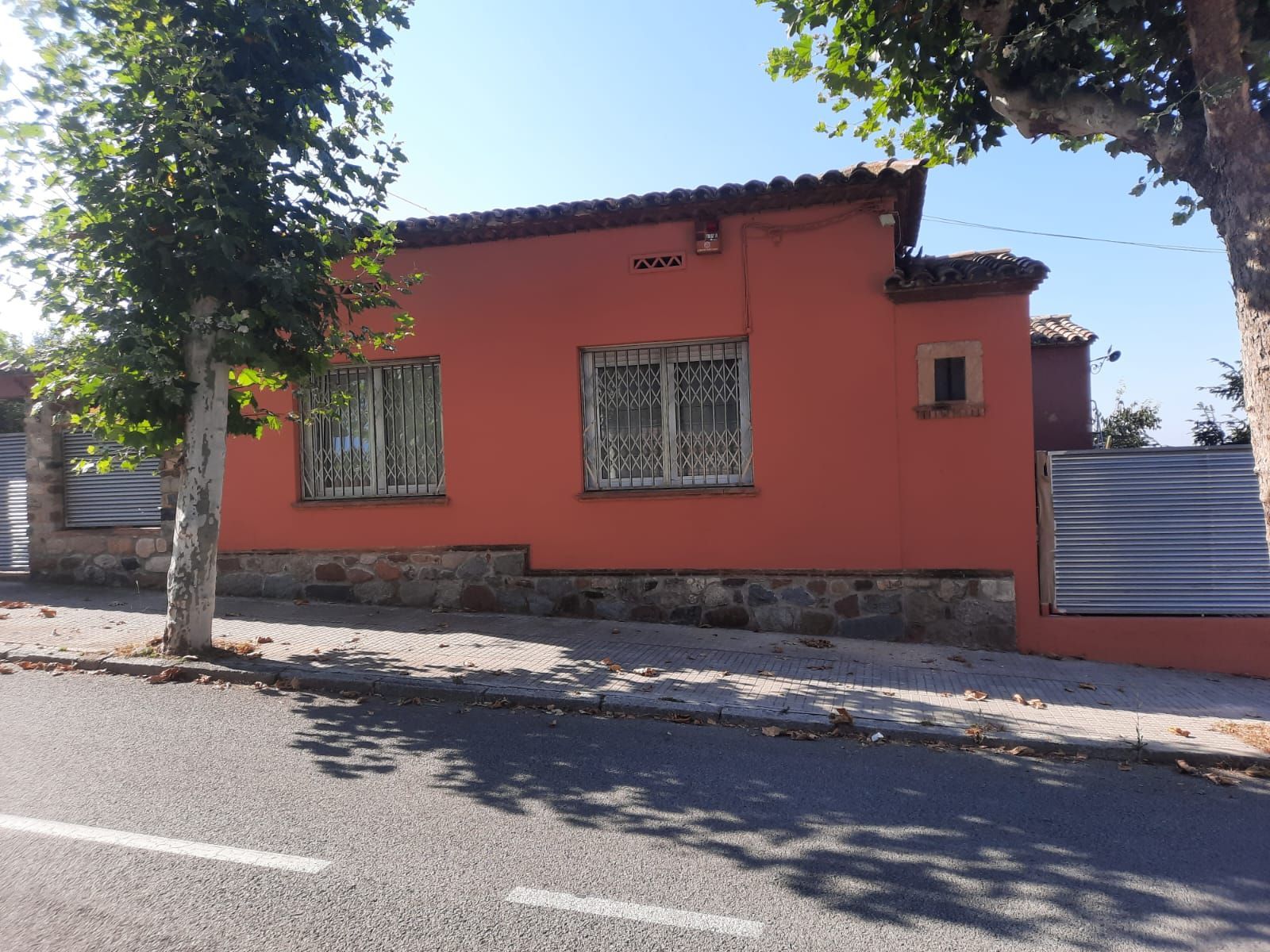 Una casa naranja con una valla y un árbol delante.