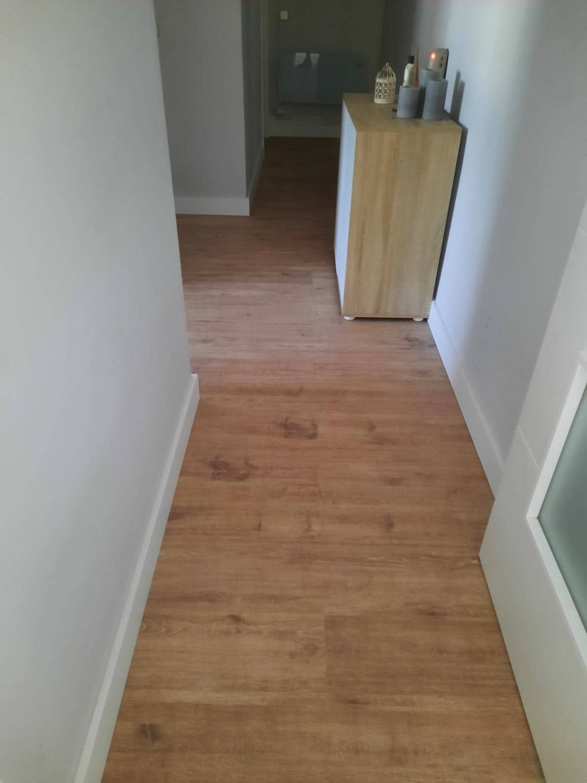 Un pasillo con suelo de madera y una cómoda en la esquina.