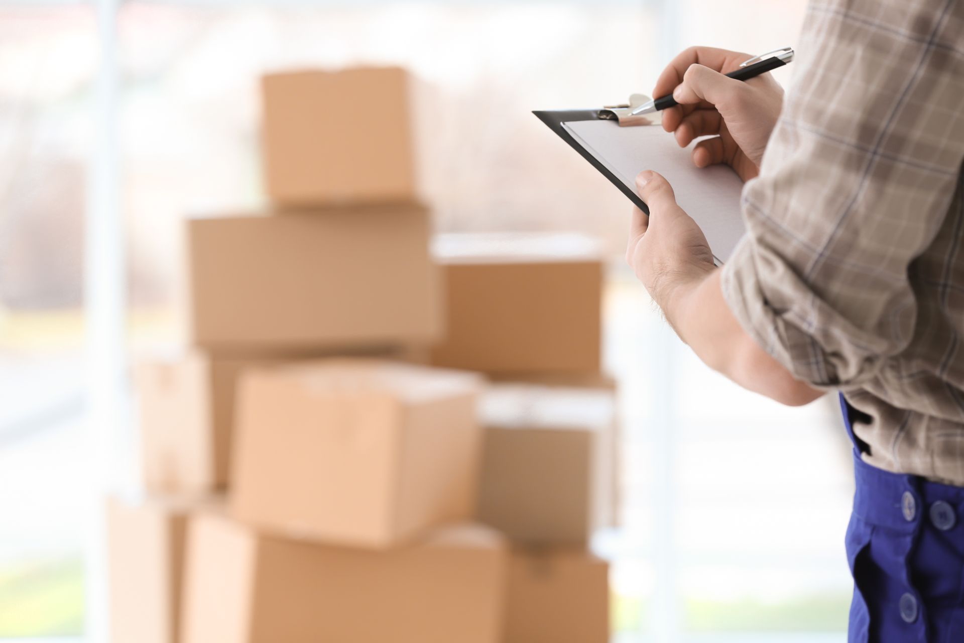 Une personne tenant un bloc-notes à côté de cartons empilés dans un entrepôt lumineux
