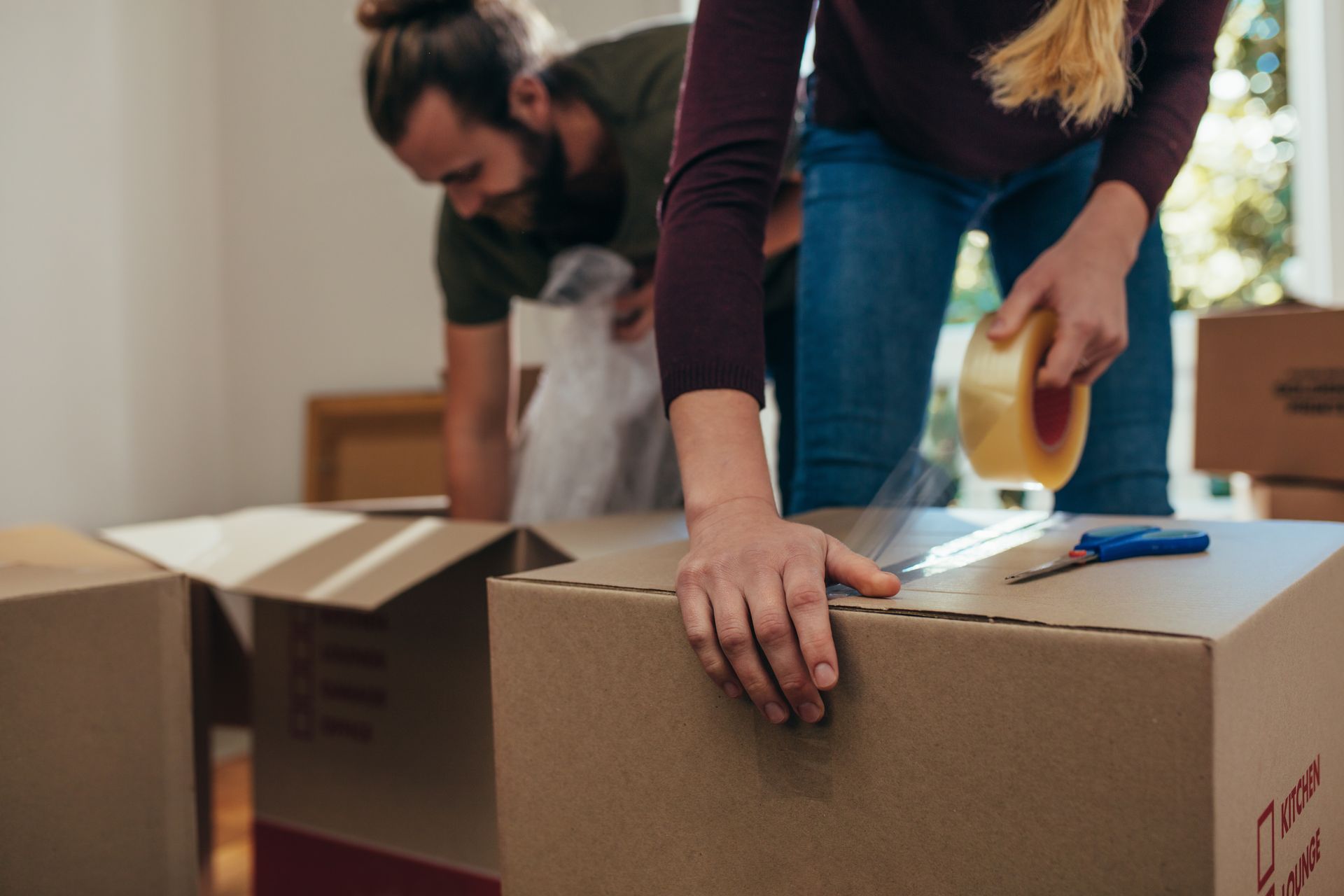 Des personnes emballent des cartons dans une pièce lumineuse, déménageant leurs affaires.