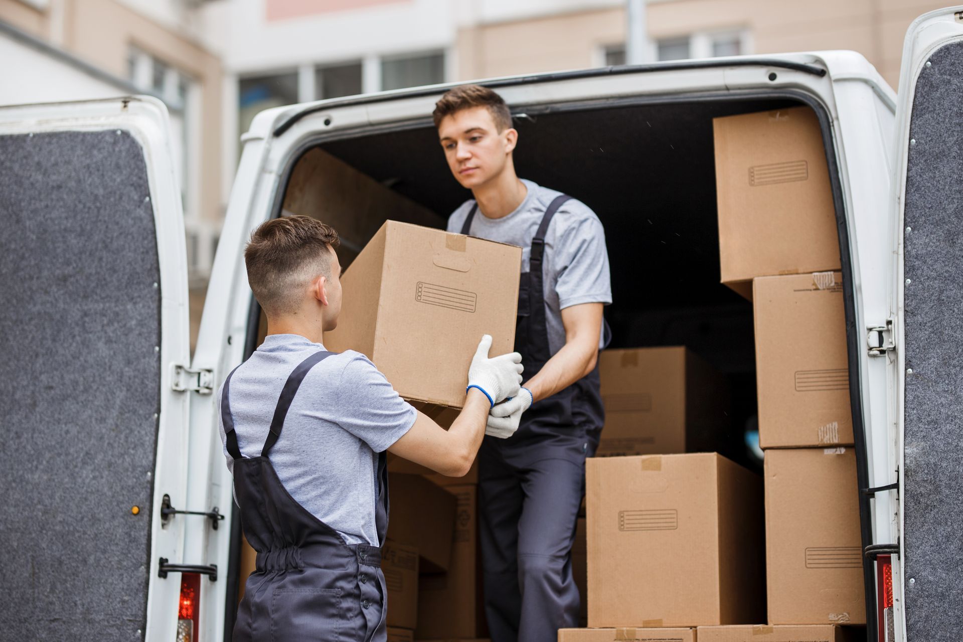 Deux déménageurs se passent des cartons entre une camionnette et l'entrée d'un immeuble.