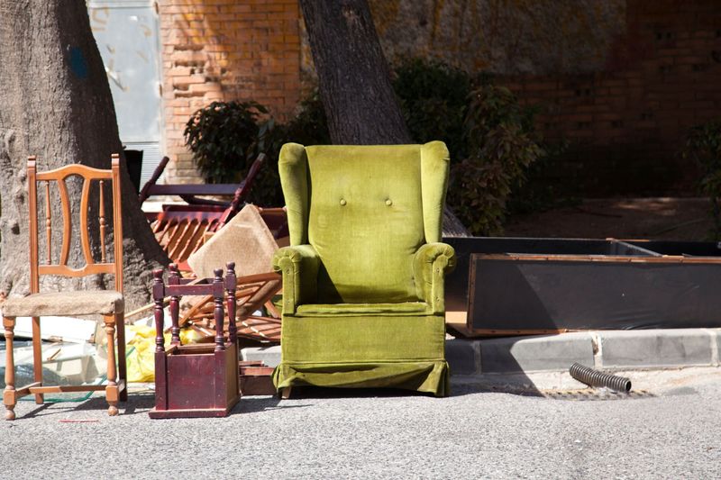 Scène extérieure avec un fauteuil vert, une chaise en bois et une petite table près d'un mur de briques