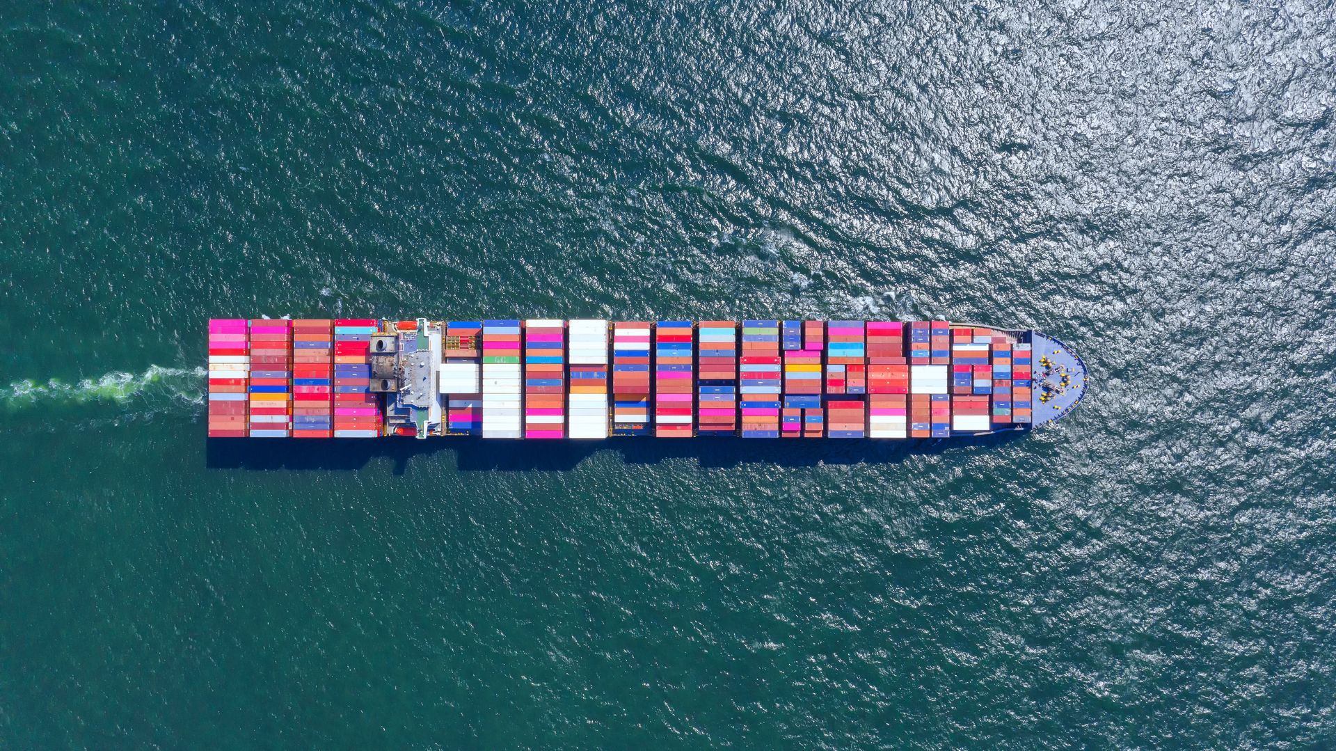 Navire porte-conteneurs chargé de conteneurs colorés sur une eau bleu foncé, vu du dessus