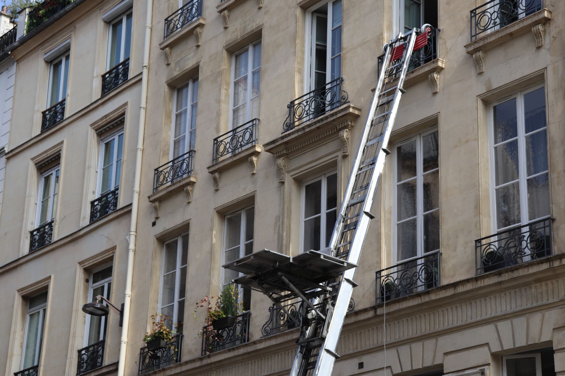 L'échelle d'un camion de pompiers est déployée sur la façade d'un immeuble parisien, avec deux personnes près du sommet.