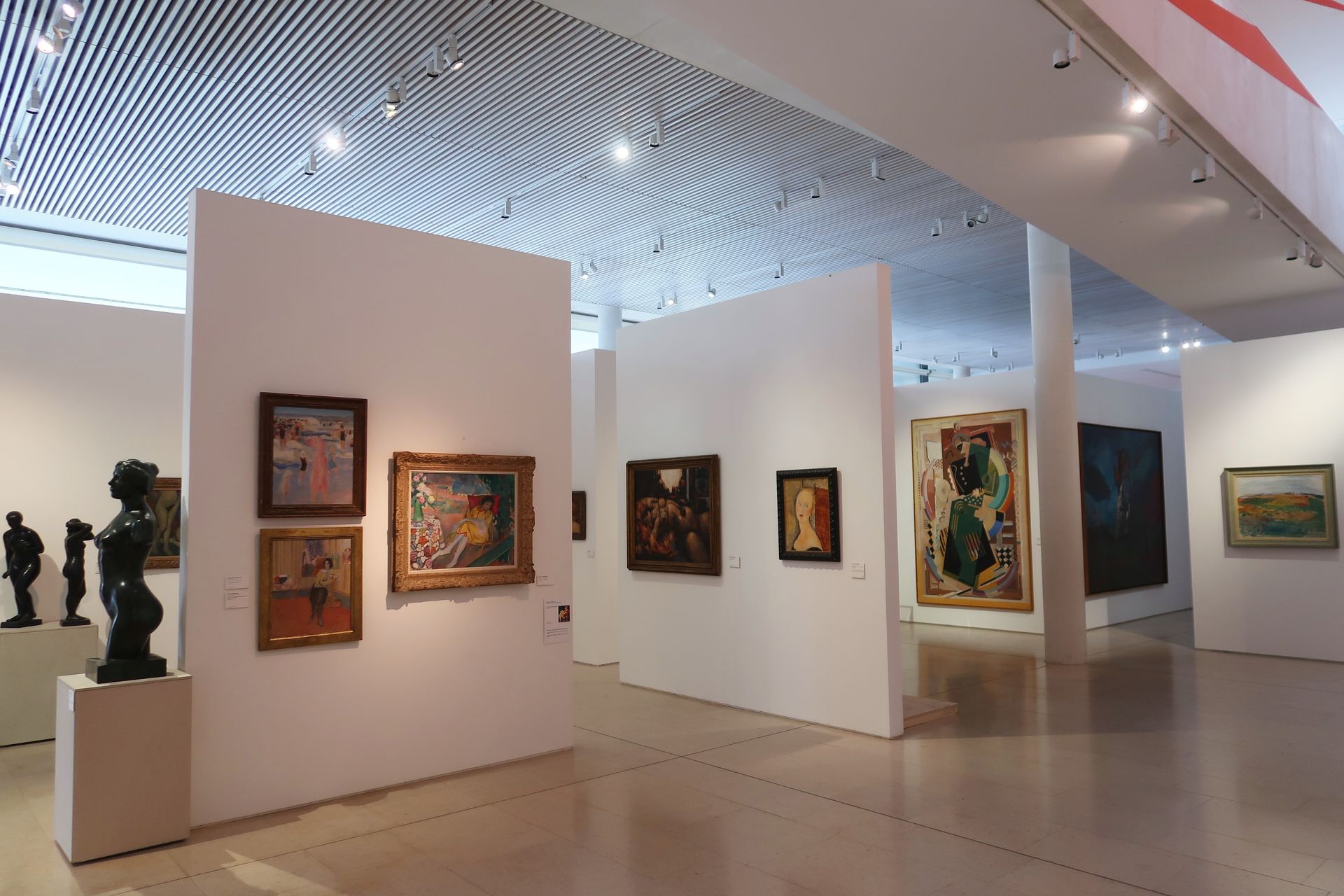 Galerie d'art moderne avec des tableaux encadrés sur des cloisons blanches et une installation au plafond