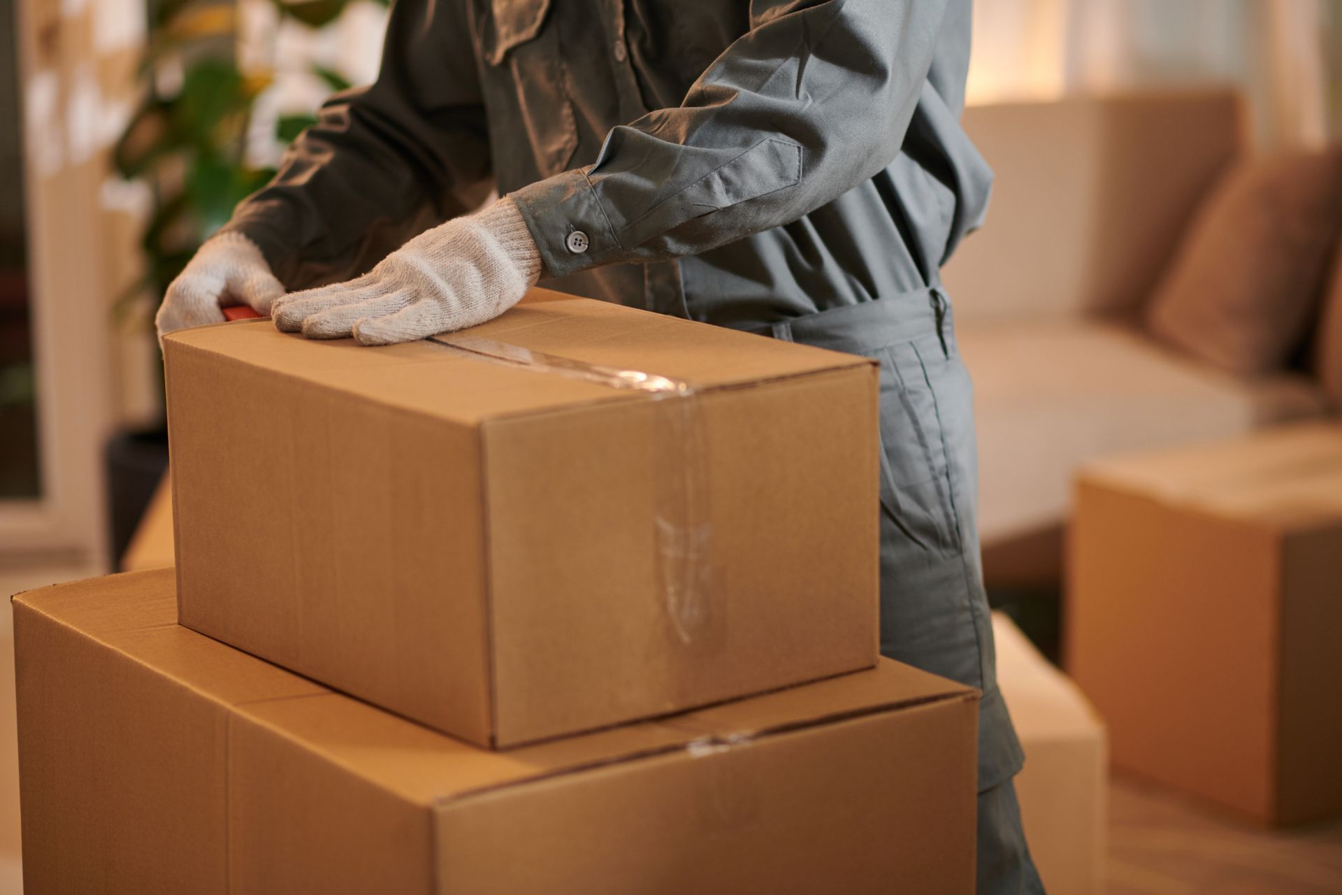 Une personne portant des gants empile des cartons de déménagement dans un salon