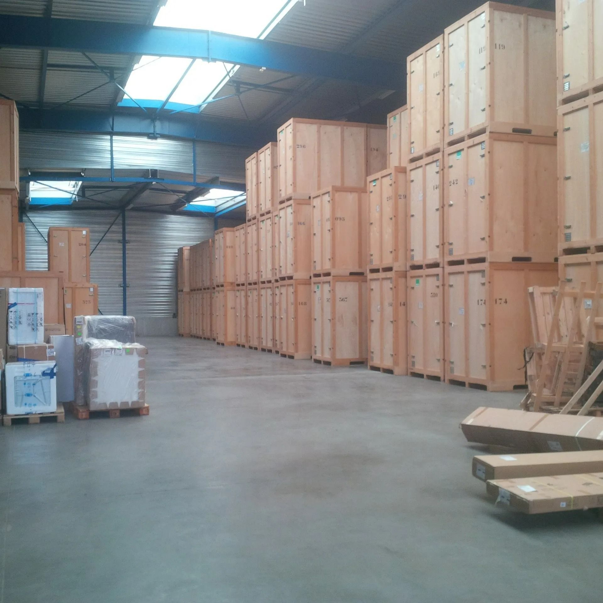 Intérieur d'entrepôt avec des caisses en bois et des palettes empilées le long d'une large allée en béton.