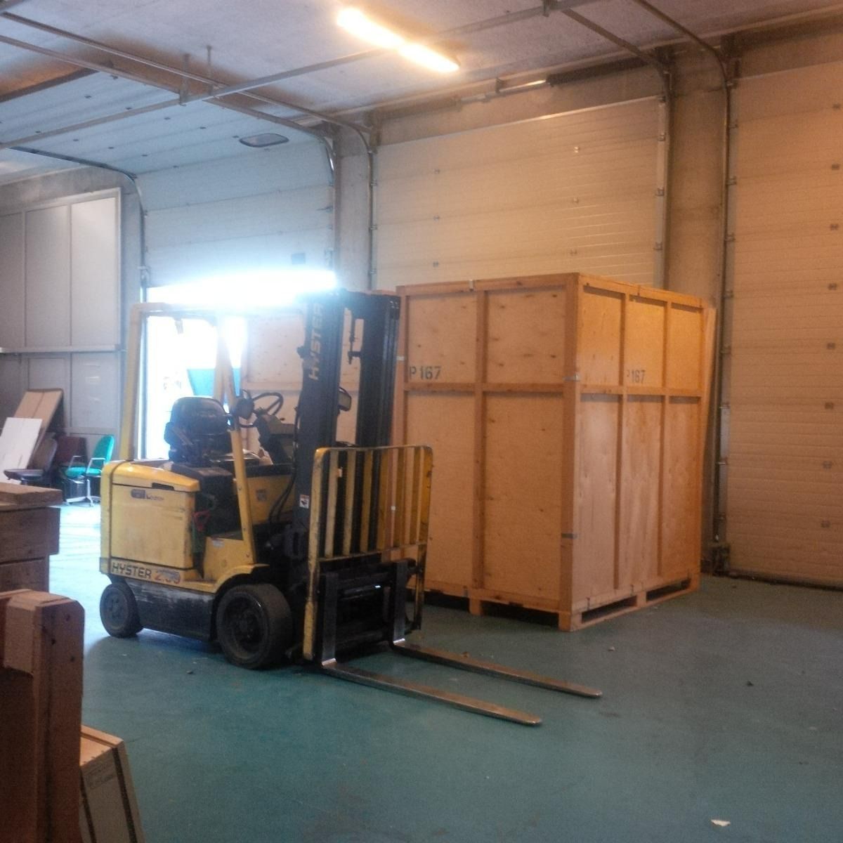 Un chariot élévateur jaune se trouve à côté d'une grande caisse en bois à l'intérieur d'un entrepôt.