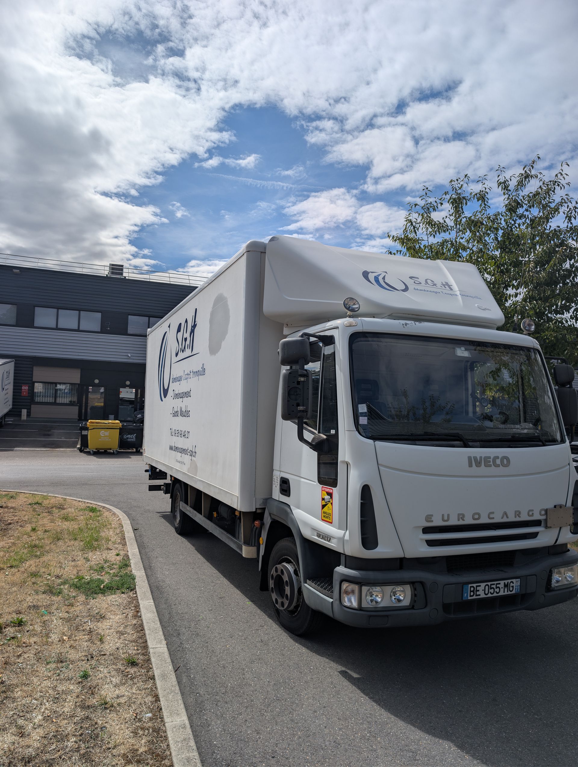 Camion de livraison blanc stationné devant un entrepôt sous un ciel nuageux