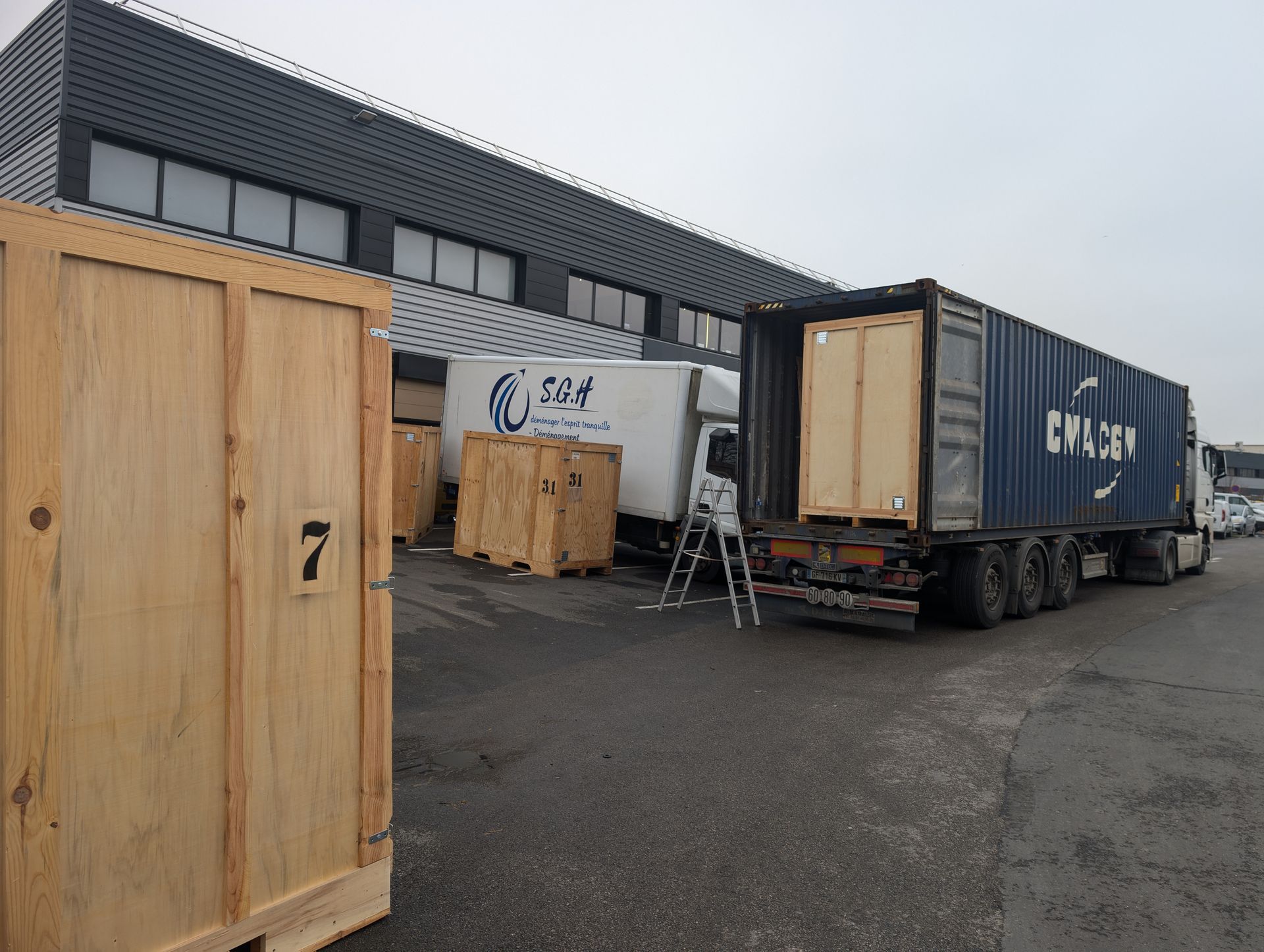 Cour d'entrepôt avec conteneurs maritimes, caisses en bois et un camion déchargeant de la marchandise