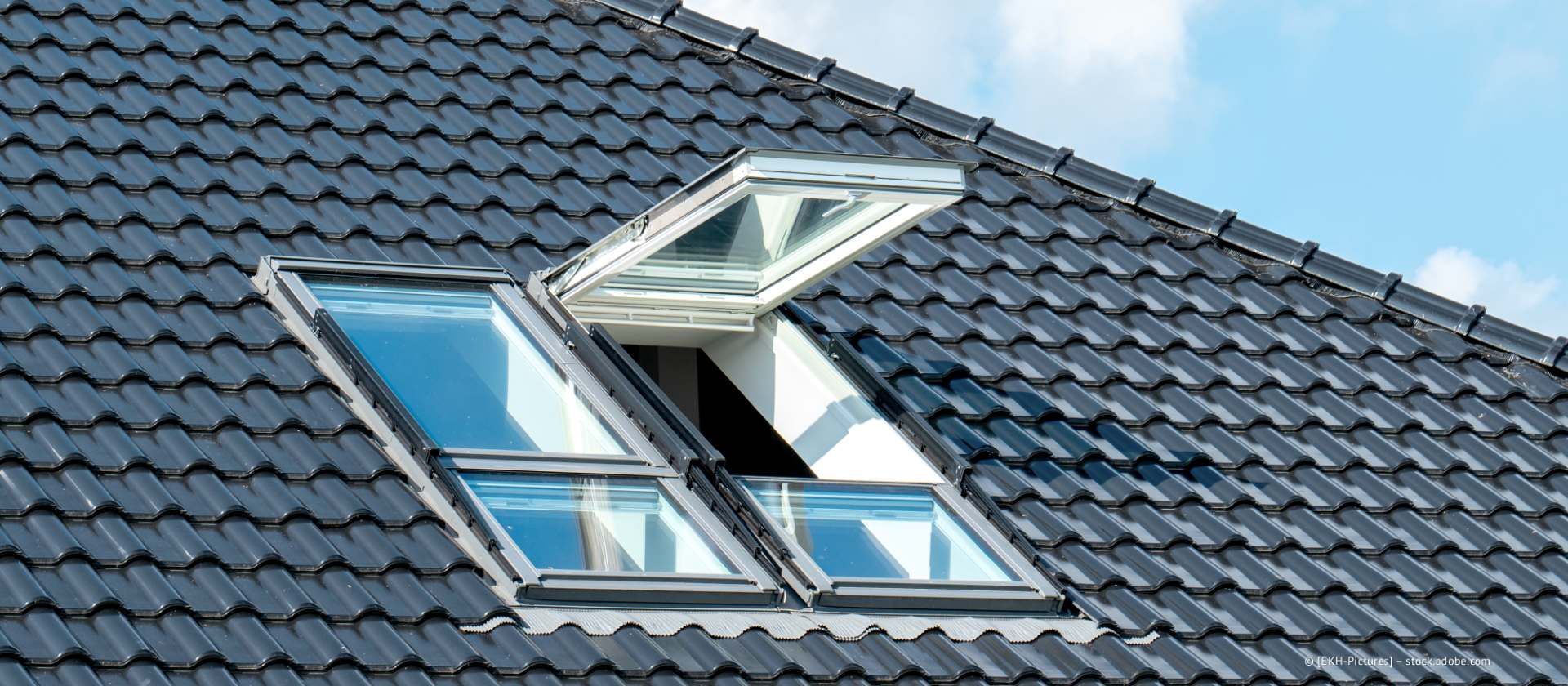 Offene Dachfenster auf einem dunkelgrauen Ziegeldach unter blauem Himmel