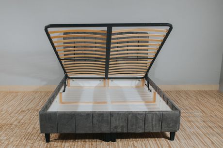 Persona colocando un colchón blanco sobre un marco de cama gris; configuración del dormitorio.