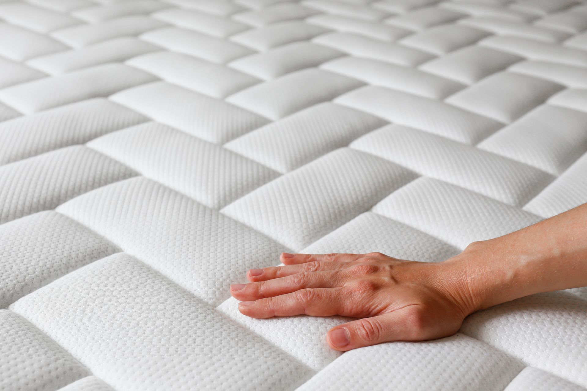 Una cama con cabecera gris, colchón blanco, dos almohadas y una manta negra. A la izquierda hay una mesita de noche.