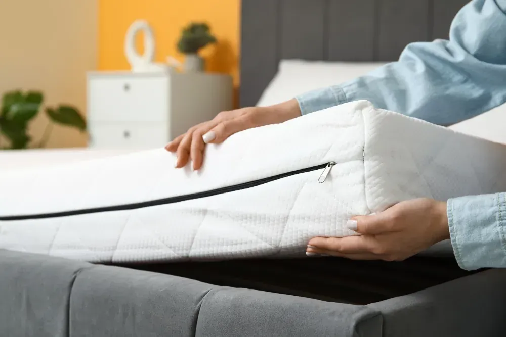 Cama king size ajustable con cabecera. Dos colchones elevados. Tonos beige, blanco y madera en un ambiente de tienda.