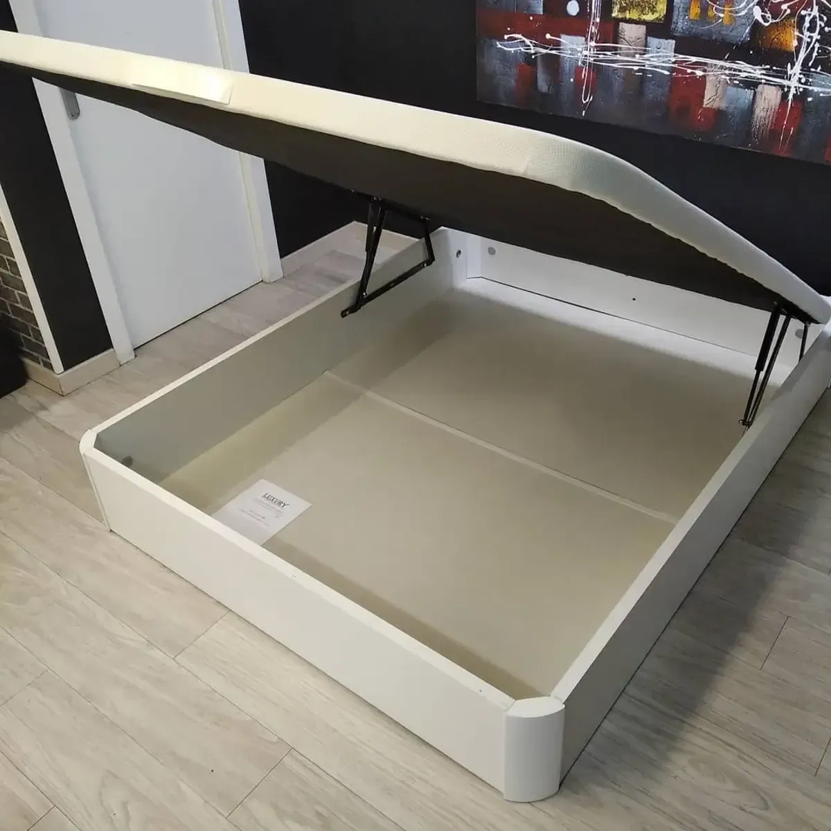 Cama blanca con almacenaje y parte superior abierta, que deja ver un compartimento vacío.