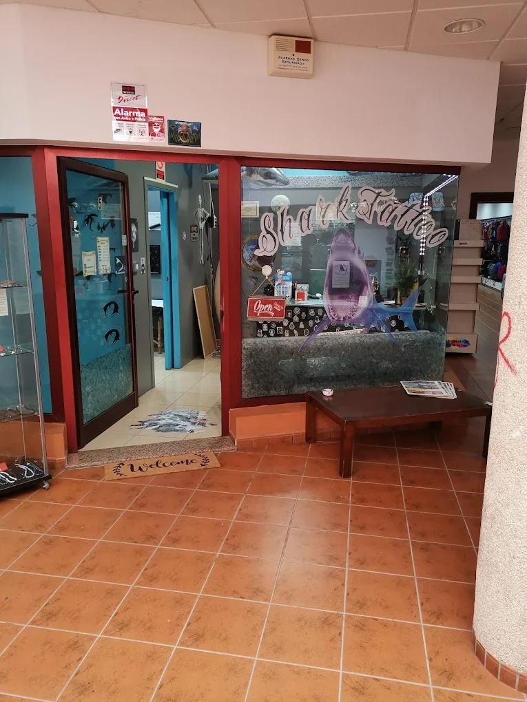 Entrada a una tienda con puertas de cristal, suelo de baldosas marrones y una pequeña zona de espera.